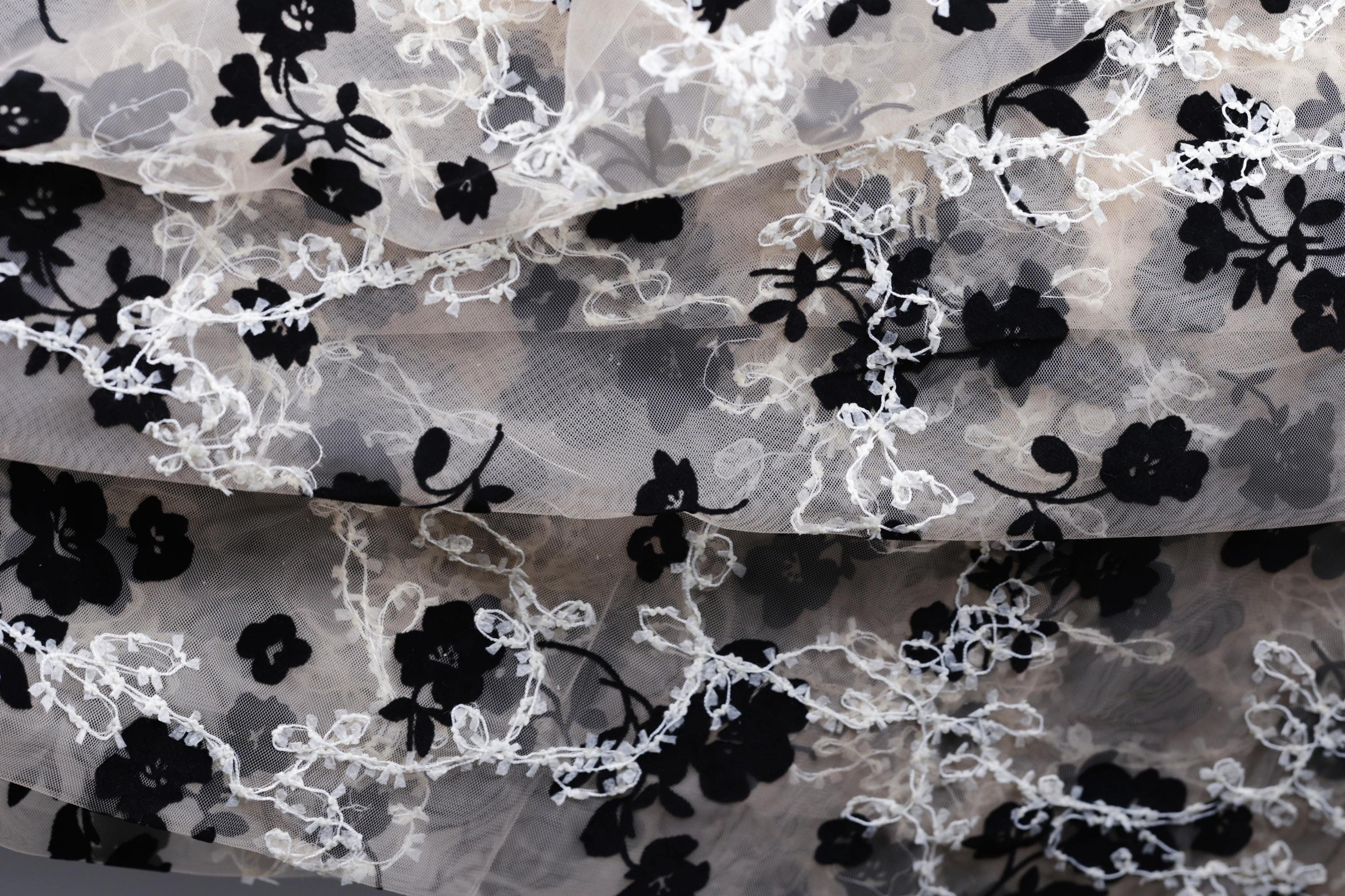 The image is a close-up of a fabric with a floral pattern, featuring black and white flowers and leaves.