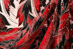 The image is a close-up of a fabric with a striking red and black pattern, featuring a repeating floral design with red leaves and black stems. The fabric appears to be made of a shiny, sequined material, adding a touch of sparkle and elegance to the design.