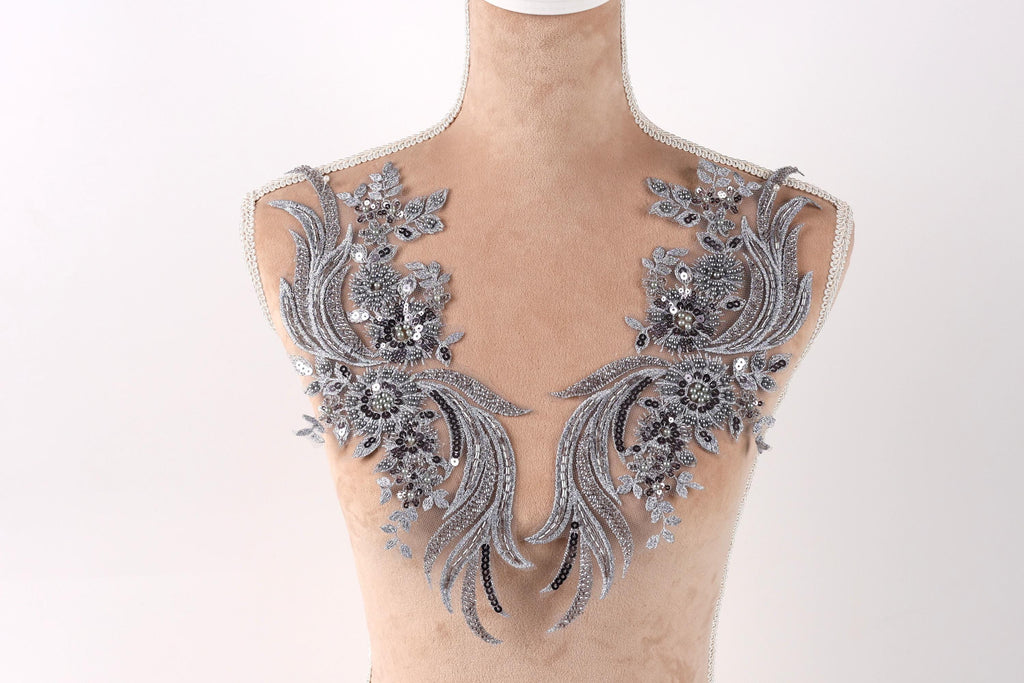 A mannequin wearing a decorative silver and black lace bodice with intricate floral and leaf designs.