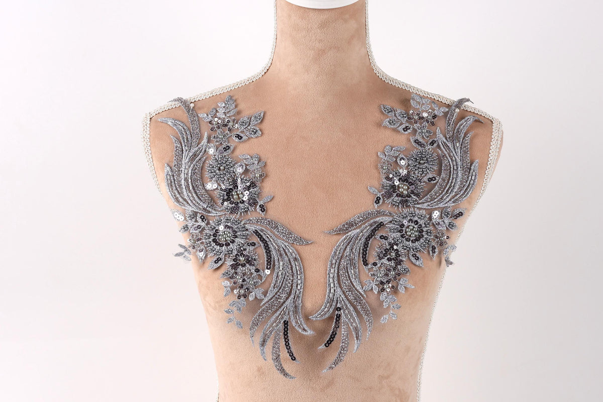 A mannequin wearing a decorative silver and black lace bodice with intricate floral and leaf designs.