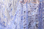 a close-up view of a fabric with a blue and white sequined pattern. The fabric appears to be a sheer material, with a delicate and intricate design.