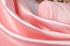 A close-up view of a soft, pink satin fabric, with a rolled-up piece of the fabric visible in the background.