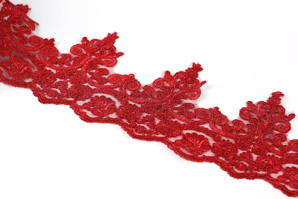 A close-up view of a red, intricately designed lace trim against a white background.