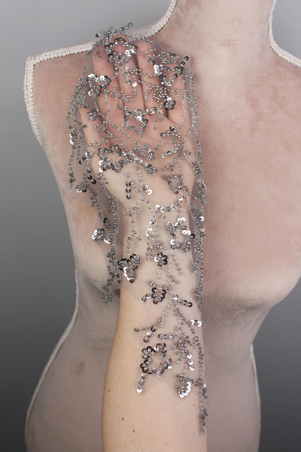 A mannequin wearing a beige dress with a delicate silver sequin overlay on the shoulder and arm.