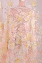 a sheer fabric with a floral pattern in shades of pink and yellow. The fabric appears to be made of sheer material, allowing light to pass through and revealing the intricate floral design.