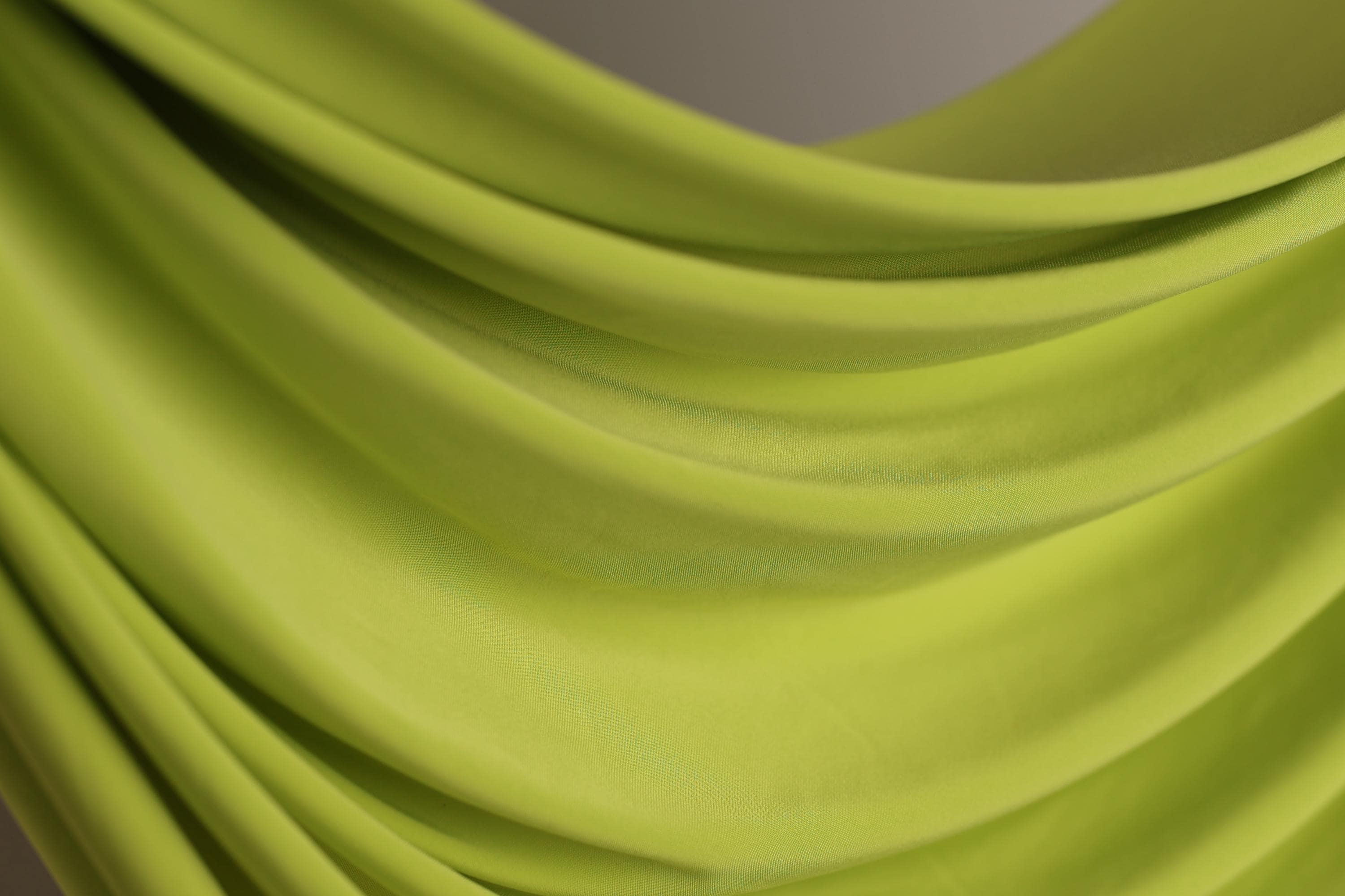 A close-up view of a bright green fabric, possibly a sheer or sheer-like material, with a soft, flowing texture.
