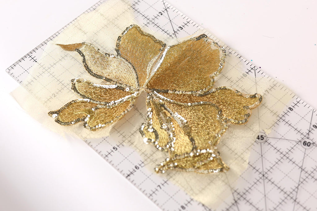 a close-up view of a gold-colored, intricately designed flower-shaped object, which appears to be a piece of embroidery or a similar decorative craft.