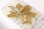 a close-up view of a gold-colored, intricately designed flower-shaped object, which appears to be a piece of embroidery or a similar decorative craft.