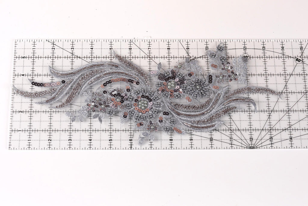 a decorative piece of fabric with intricate silver and black embroidered designs, including a floral pattern and a wave-like motif.