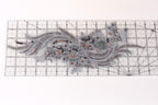 a decorative piece of fabric with intricate silver and black embroidered designs, including a floral pattern and a wave-like motif.