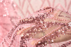 A close-up view of a hand holding a piece of pink sequin fabric, with the fabric's intricate details and shimmering beads visible.