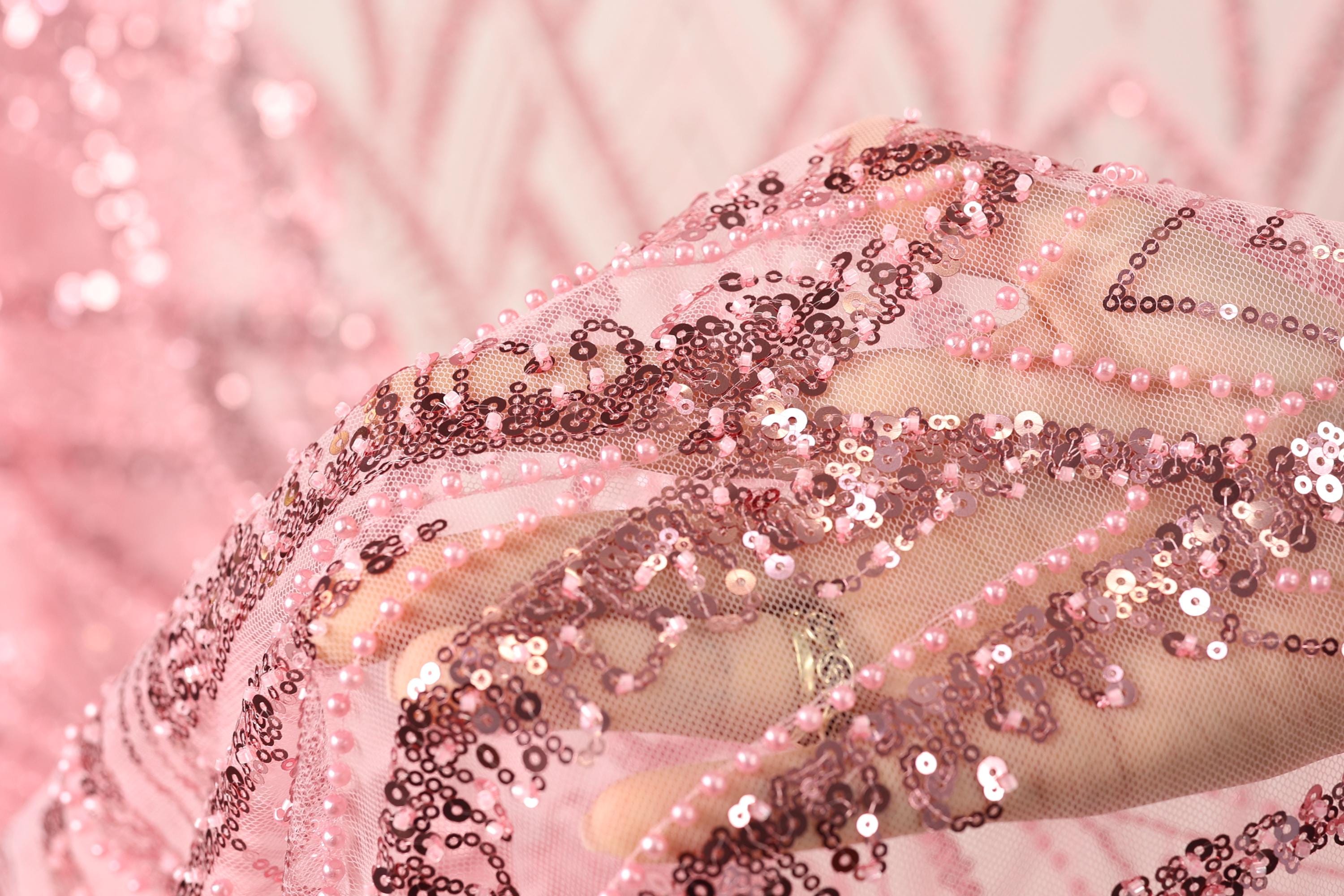 A close-up view of a hand holding a piece of pink sequin fabric, with the fabric's intricate details and shimmering beads visible.