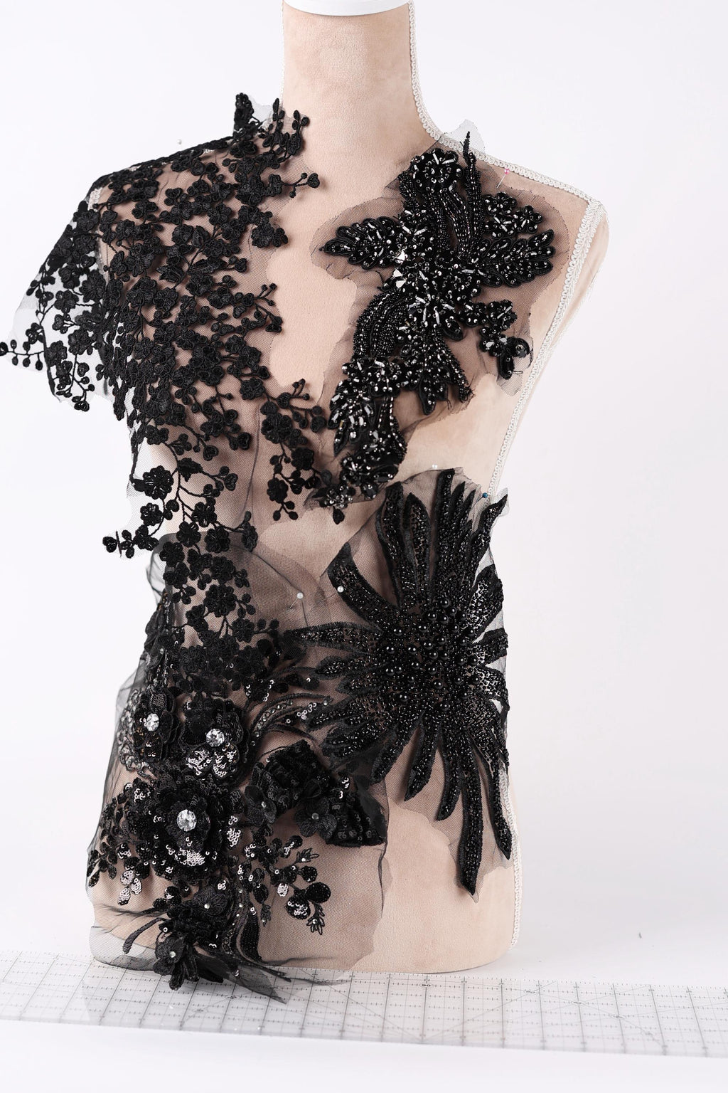 A mannequin wearing a black dress with intricate lace and floral embellishments.