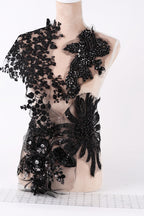 A mannequin wearing a black dress with intricate lace and floral embellishments.
