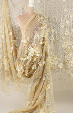 a mannequin wearing a gold sequin dress with a sheer, flower-like design. The dress has a long, flowing skirt and a sheer overlay, creating a shimmering effect. The dress appears to be made of sheer fabric, which adds to its delicate and elegant appearance.