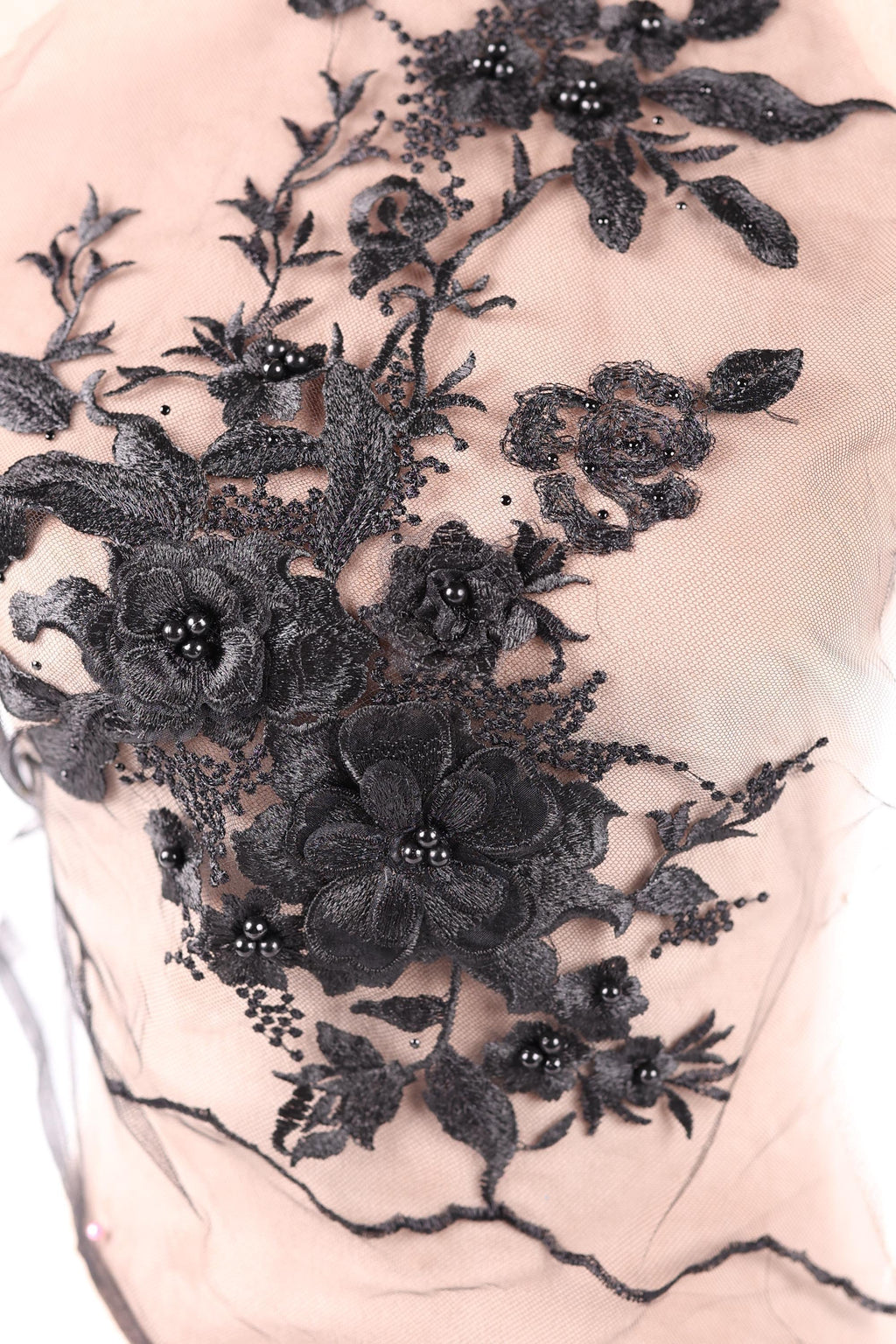 a close-up view of a delicate, intricate black lace design with floral elements. The lace appears to be made of a soft, delicate material, possibly silk or chiffon, and is adorned with black beads or sequins that add a touch of sparkle and elegance to the overall design. The floral elements are arranged in a way that creates a visually appealing and harmonious composition.