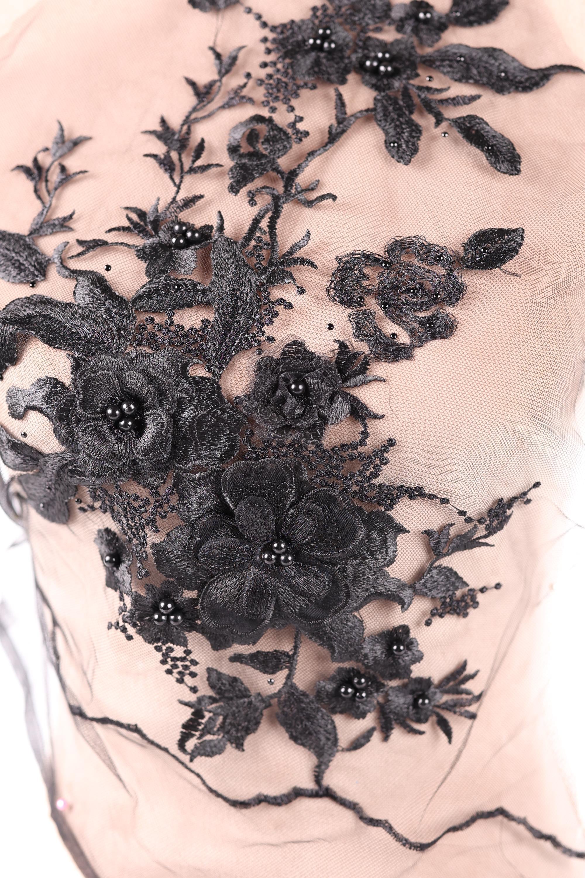 a close-up view of a delicate, intricate black lace design with floral elements. The lace appears to be made of a soft, delicate material, possibly silk or chiffon, and is adorned with black beads or sequins that add a touch of sparkle and elegance to the overall design. The floral elements are arranged in a way that creates a visually appealing and harmonious composition.