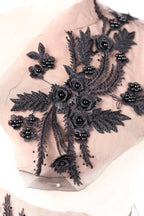 a close-up view of a delicate, intricate black lace design with numerous black flowers and leaves. The design is composed of numerous black flowers and leaves, creating a striking contrast against the light-colored background. The black lace appears to be meticulously crafted, with each flower and leaf carefully placed to create a visually appealing and detailed pattern.