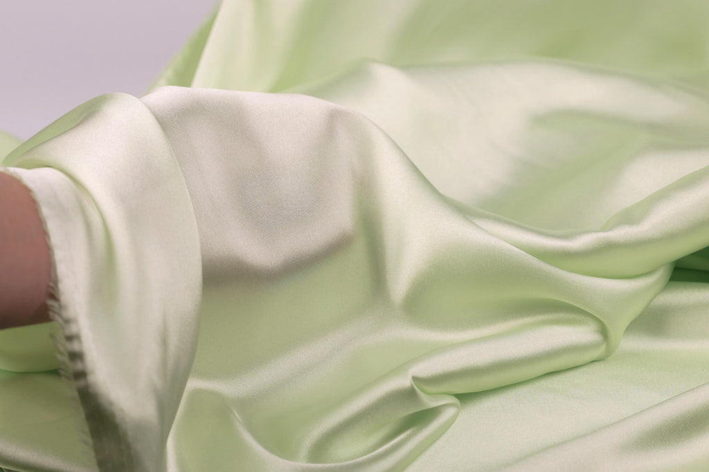 A close-up view of a soft, flowing green satin fabric, with a blurred background.
