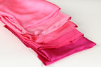 A stack of four pink satin fabric pieces is neatly arranged on a white surface.