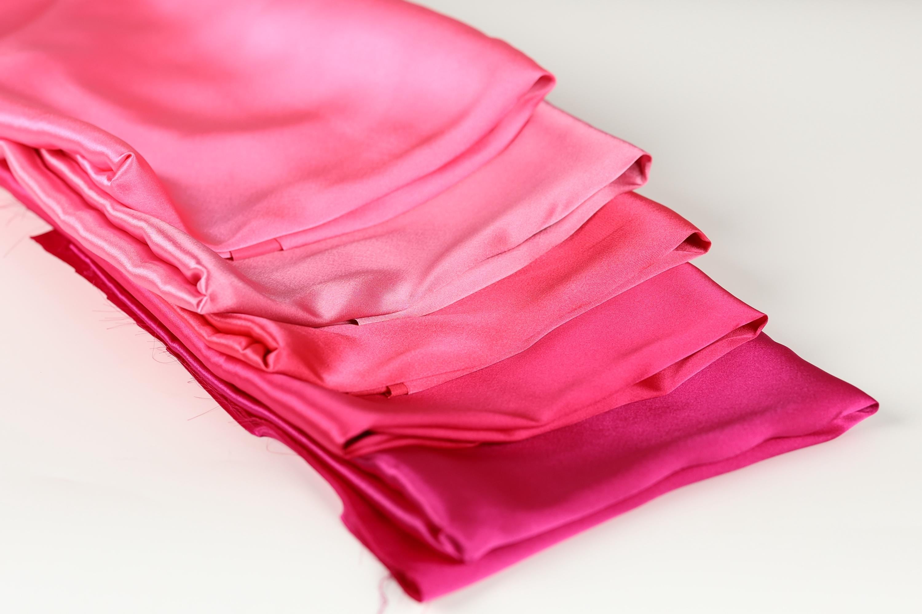 A stack of four pink satin fabric pieces is neatly arranged on a white surface.