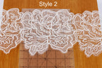 a close-up view of a delicate white lace pattern, with the intricate details of the lace visible. The lace appears to be a part of a larger design, as it is placed on a wooden surface. A ruler is also present in the image, likely used for measuring or marking the lace pattern.