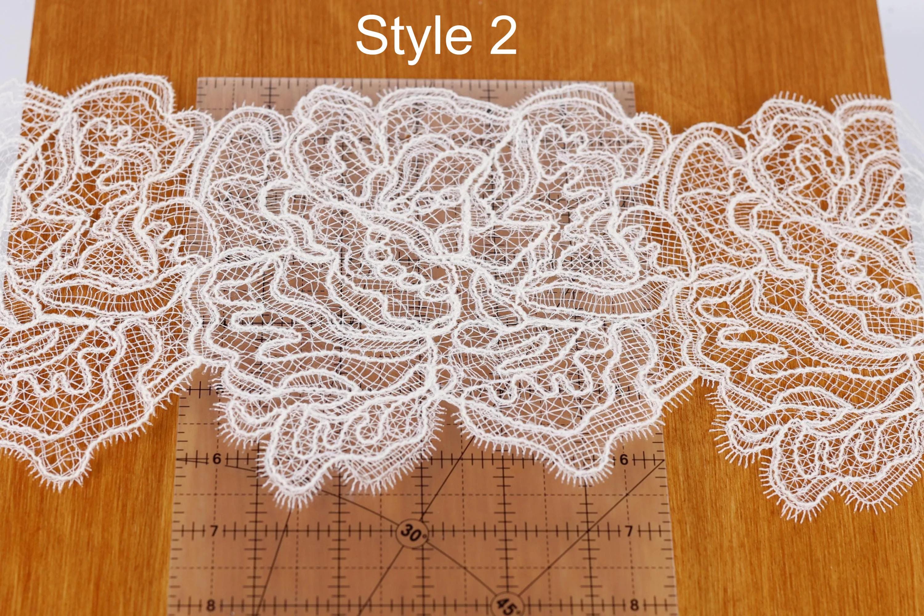 a close-up view of a delicate white lace pattern, with the intricate details of the lace visible. The lace appears to be a part of a larger design, as it is placed on a wooden surface. A ruler is also present in the image, likely used for measuring or marking the lace pattern.
