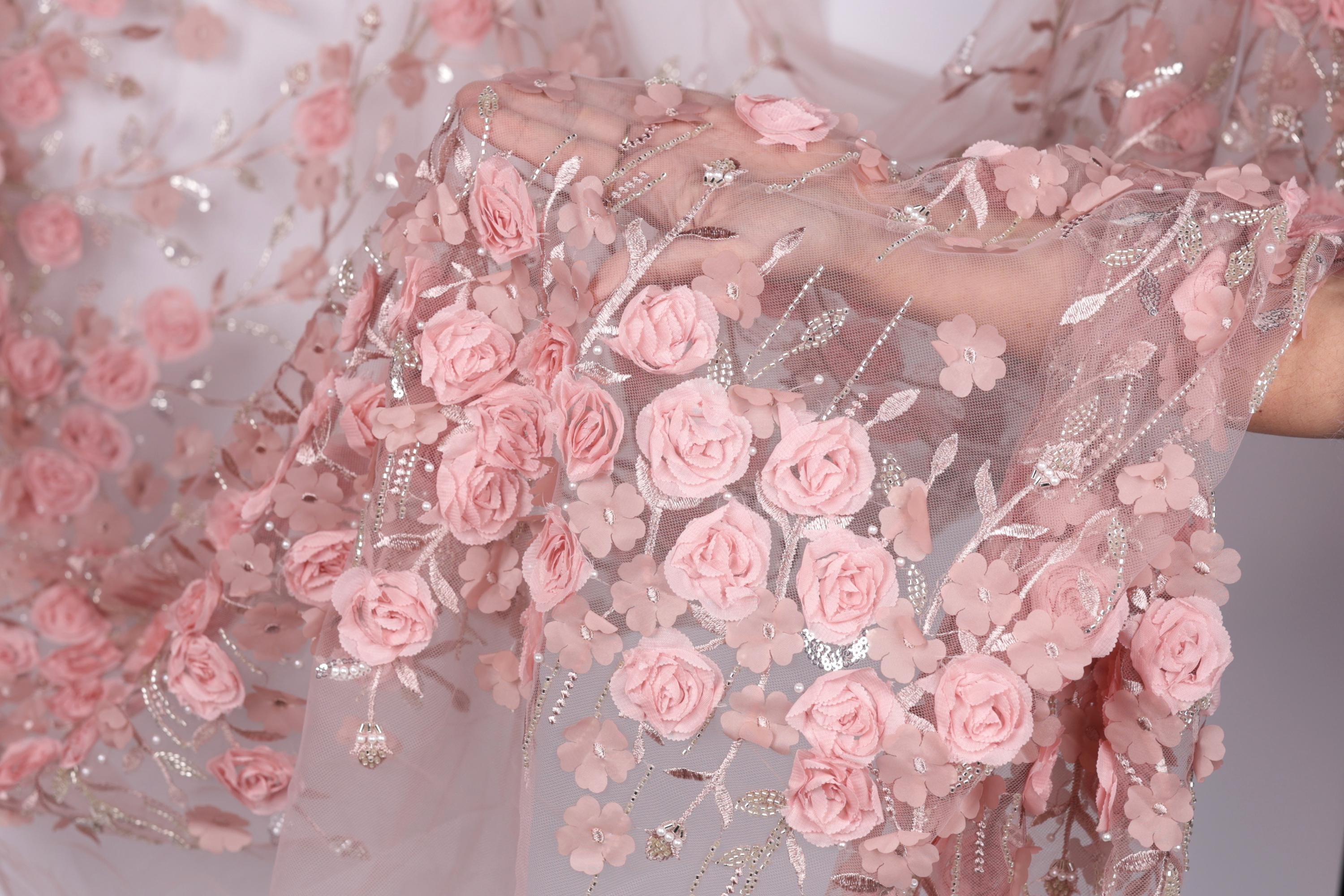 A close-up view of a delicate, pink floral fabric with numerous small pink roses and leaves attached to it.