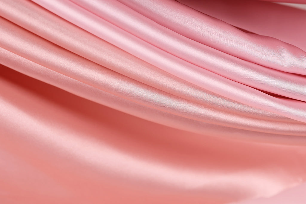 A close-up view of a soft, flowing pink fabric, possibly silk or satin, with a smooth and shiny texture.