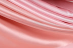 A close-up view of a soft, flowing pink fabric, possibly silk or satin, with a smooth and shiny texture.