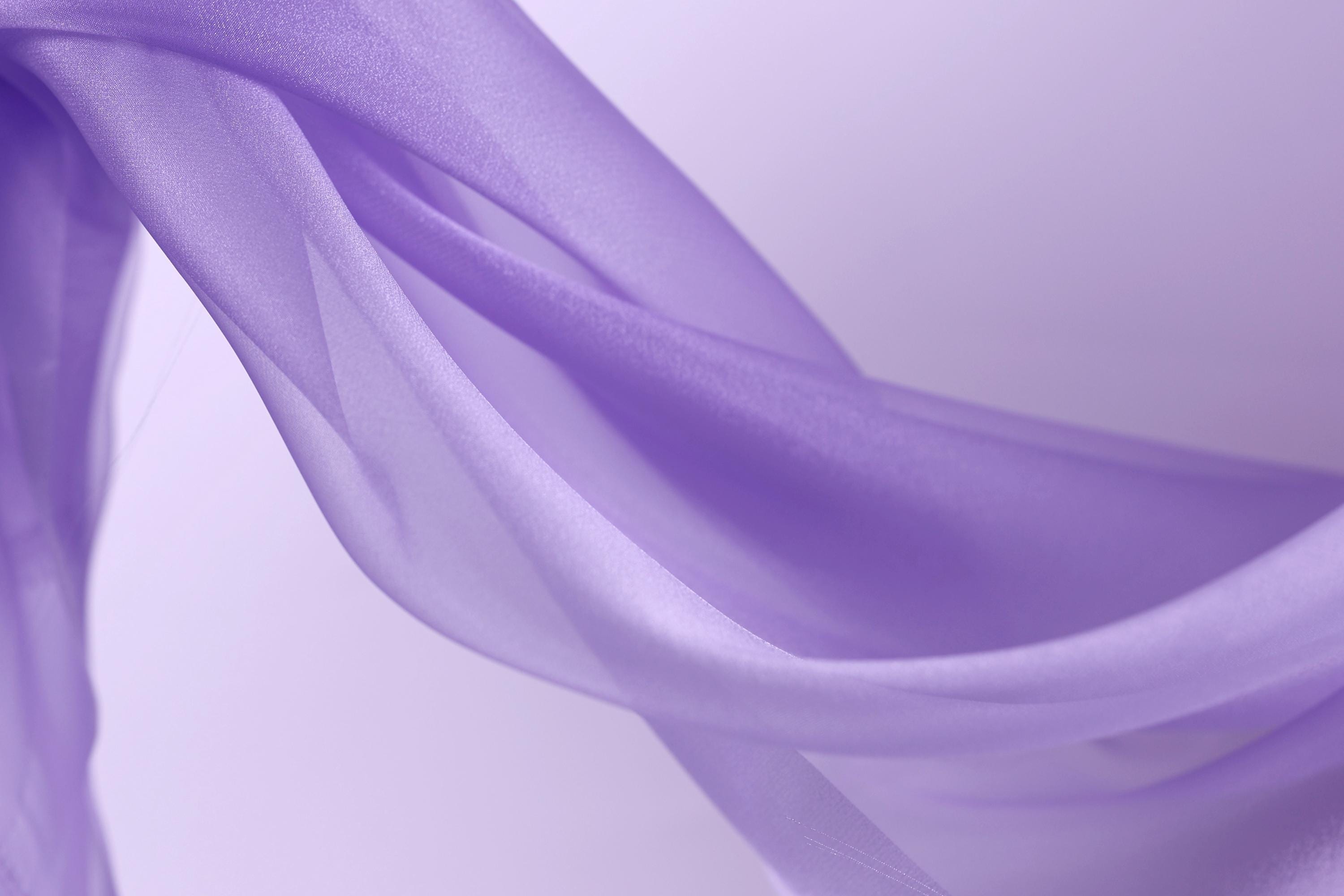 The image is a close-up of a flowing, purple fabric, possibly silk or chiffon, with a soft, delicate texture.
