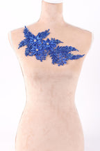 A mannequin wearing a beige dress with a blue floral embellishment on the chest area.