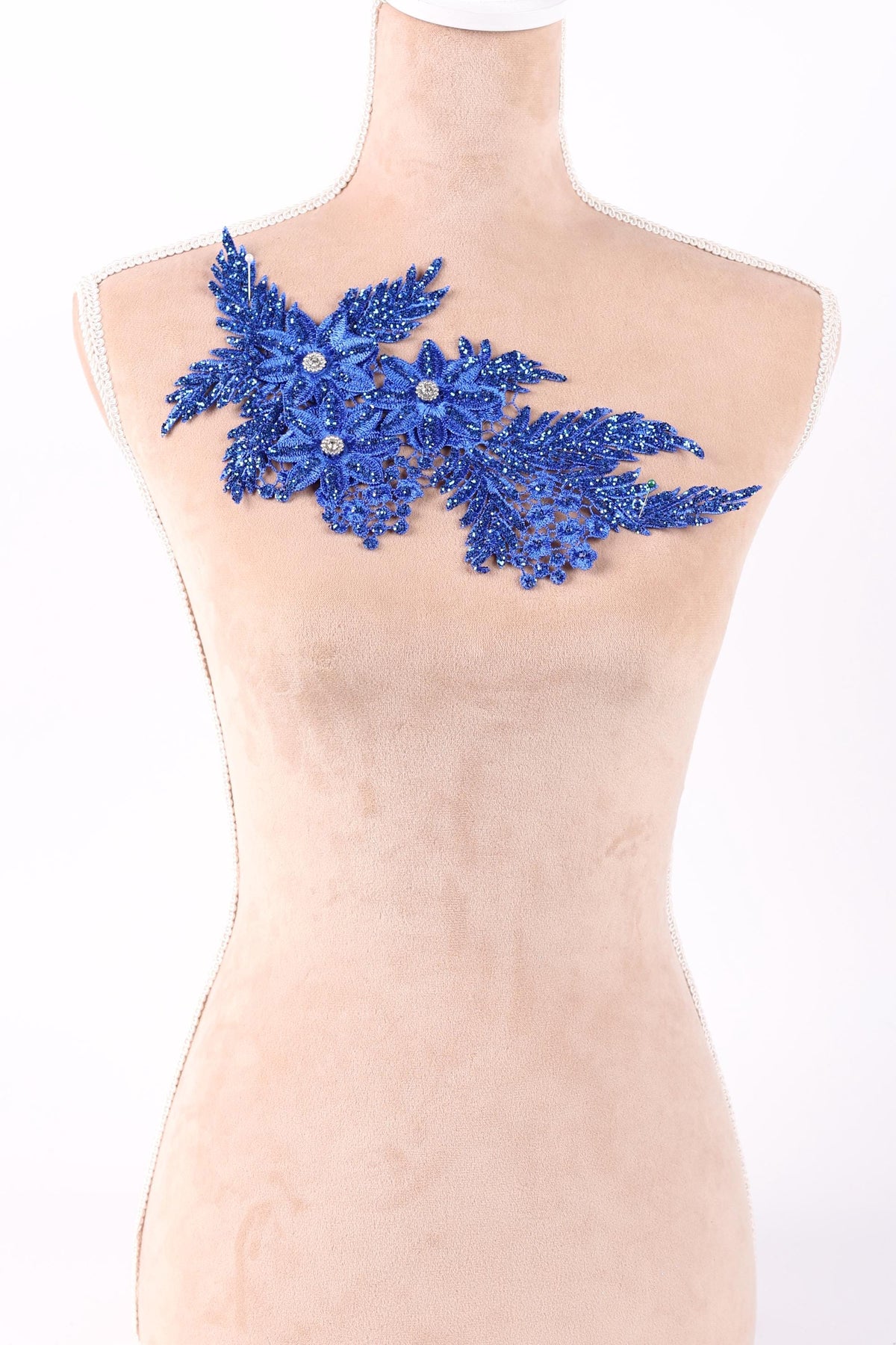 A mannequin wearing a beige dress with a blue floral embellishment on the chest area.