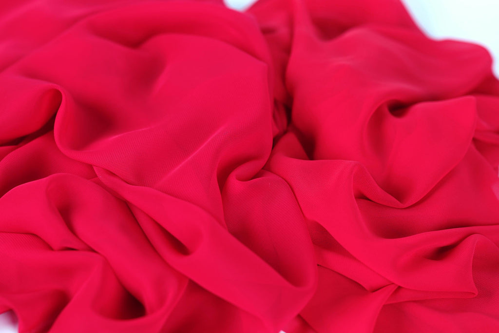 The image is a close-up of a red fabric, possibly silk or chiffon, with a crumpled and wrinkled texture.