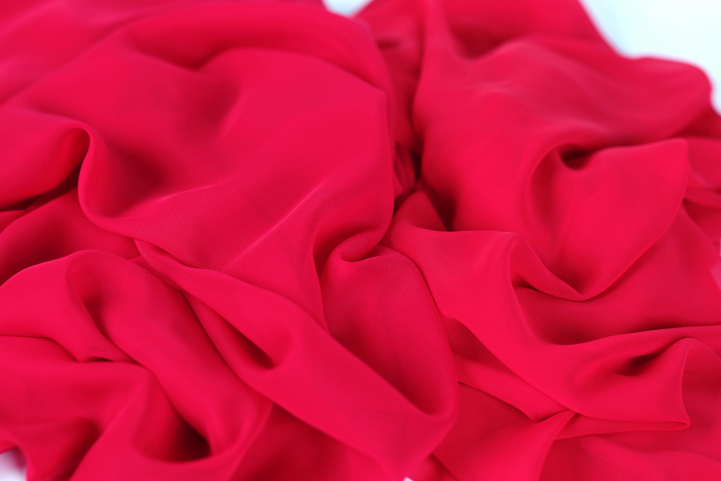 The image is a close-up of a red fabric, possibly silk or chiffon, with a crumpled and wrinkled texture.