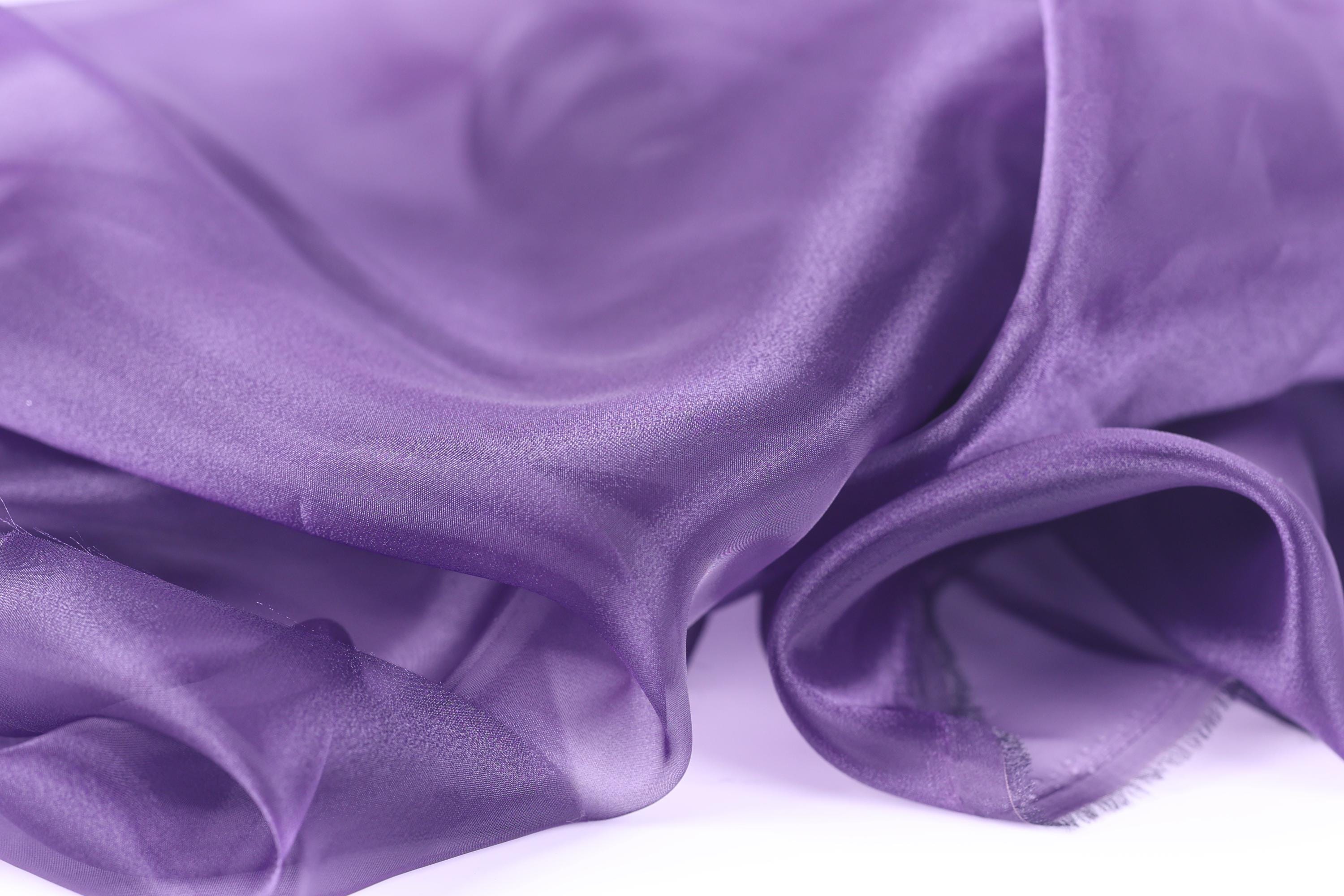 a close-up view of a soft, flowing purple fabric, possibly silk or chiffon, with a smooth and shiny texture.