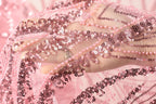 A close-up view of a hand holding a piece of pink and black sequin fabric.