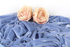 Two light pink roses resting on a crumpled blue fabric.