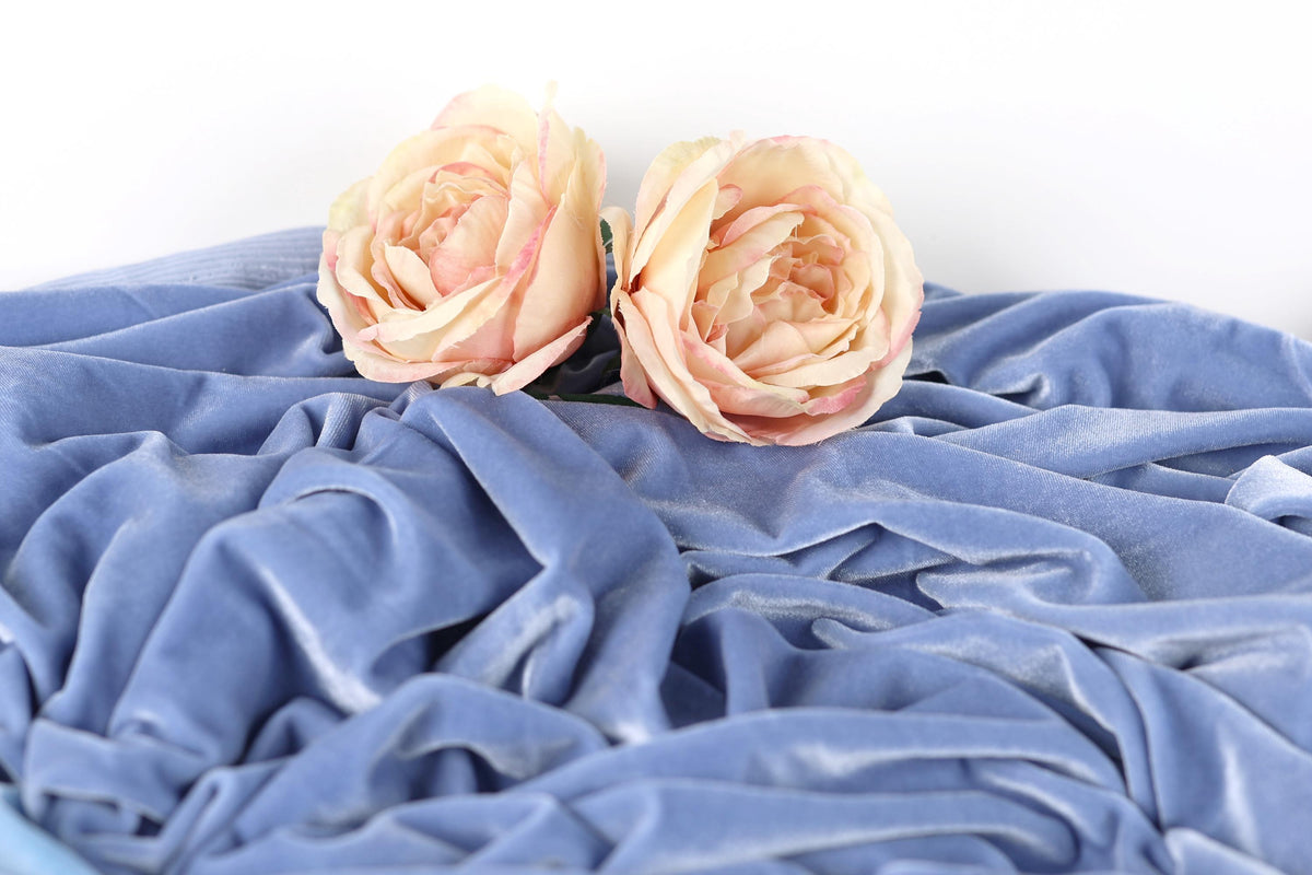 Two light pink roses resting on a crumpled blue fabric.