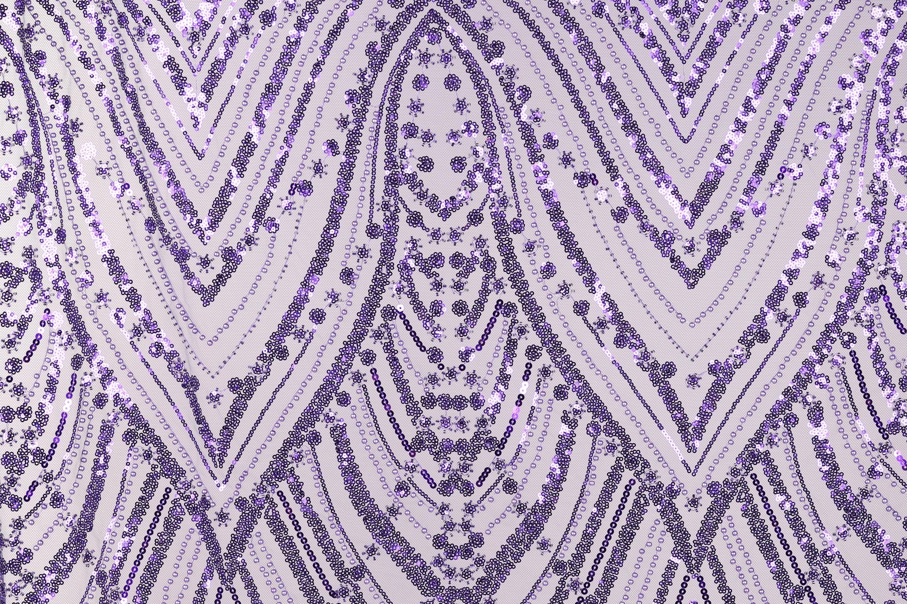 a close-up view of a fabric with a repeating pattern of purple and white sequins. The pattern consists of diagonal lines and curves, creating a visually striking and intricate design. The fabric appears to be made of a material that has a shiny, sequined texture, adding a touch of sparkle and elegance to the overall appearance.