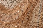 The image is a close-up of a fabric with a gold and black sequin pattern, featuring a mix of small and large sequins arranged in a zigzag pattern.