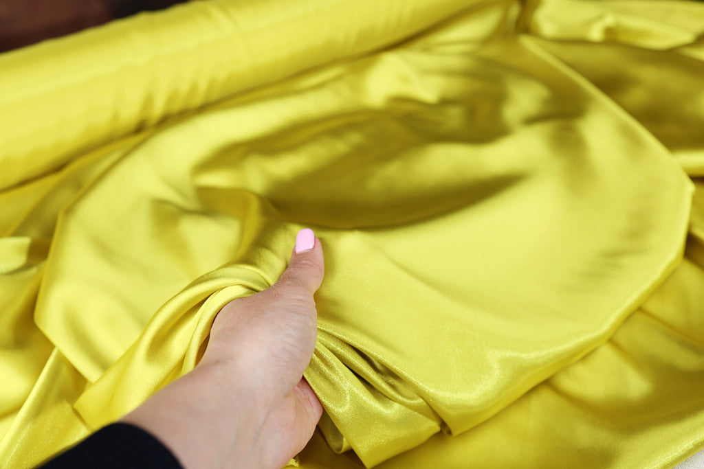 A hand is holding a piece of yellow fabric, possibly silk, and examining it closely.