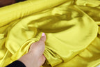 A hand is holding a piece of yellow fabric, possibly silk, and examining it closely.