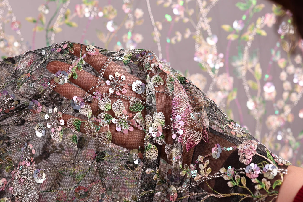 A close-up view of a hand holding a piece of fabric with intricate floral embroidery and sequins.