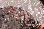 A close-up view of a hand holding a piece of fabric with intricate floral embroidery and sequins.