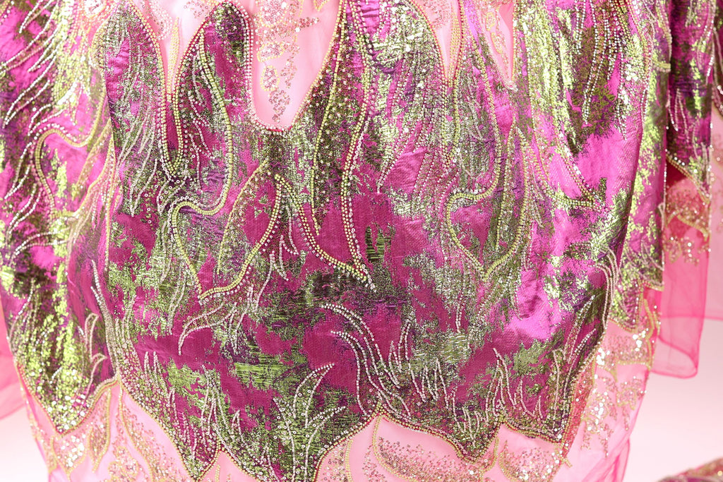 a close-up view of a fabric with a vibrant, colorful pattern of pink and green sequins and beads. The fabric appears to be a piece of clothing or textile, with the intricate design and texture visible.
