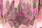 a close-up view of a fabric with a vibrant, colorful pattern of pink and green sequins and beads. The fabric appears to be a piece of clothing or textile, with the intricate design and texture visible.