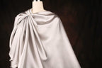 A mannequin wearing a gray satin cape with a draped, flowing design.