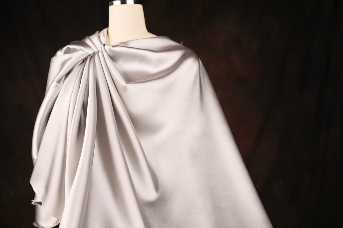 A mannequin wearing a gray satin cape with a draped, flowing design.