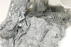 a close-up view of a delicate, intricately designed fabric with a silver and gray color scheme. The fabric appears to be made of lace or a similar material, with a floral or leaf-like pattern visible on the surface. The fabric is crumpled and wrinkled, giving it a textured and somewhat messy appearance.